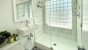 Un baño moderno con ducha de vidrio, lavamanos blanco y espejo sobre él.