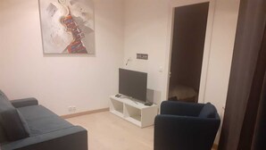Un salon avec un canapé, un fauteuil, un téléviseur posé sur un meuble et une porte.