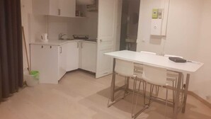 Une cuisine compacte avec des meubles blancs, un plan de travail blanc et un tabouret de bar.