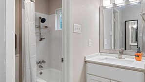 A bathroom with a bathtub, a shower with a glass enclosure, a white vanity with a mirror, and a hand soap dispenser. - Cozy chic studio close to Downtown and Domain (Austin)
