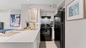 A modern kitchen with white cabinets, a black refrigerator, and a stainless steel sink. - Cozy chic studio close to Downtown and Domain (Austin)