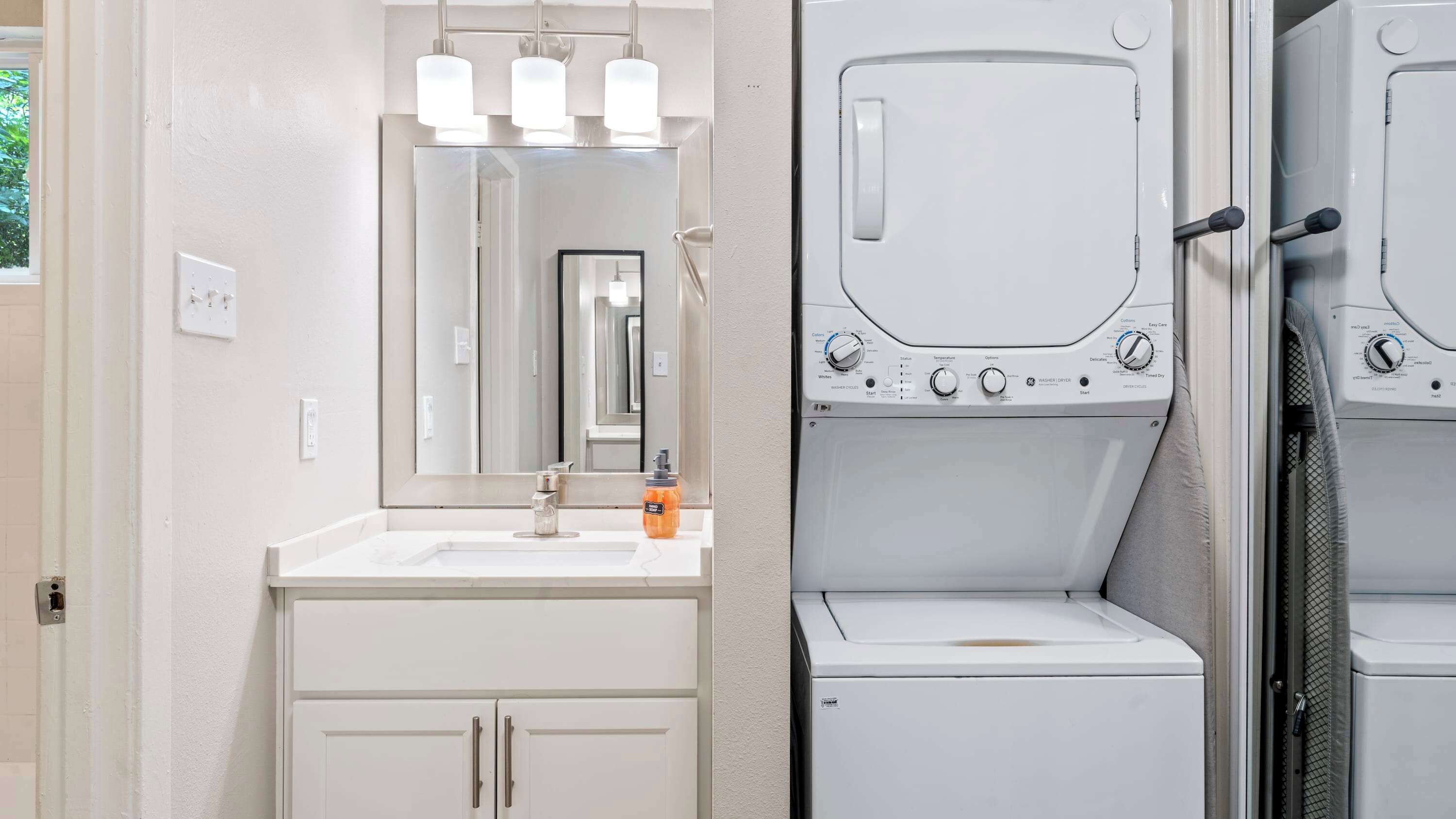 A modern bathroom with a sink, mirror, and two stacked washing machines.
