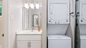 Casa de banho moderna com lavatório, espelho e duas máquinas de lavar roupa empilhadas.