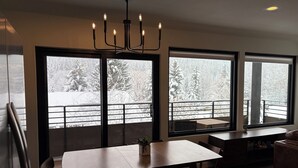 Un comedor moderno con una mesa grande y sillas, una araña y ventanas amplias con vistas a un paisaje nevado.