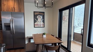 Una cocina moderna con un refrigerador de acero inoxidable, armarios de madera, una mesa de comedor con sillas y un ventanal con vistas a un paisaje nevado.