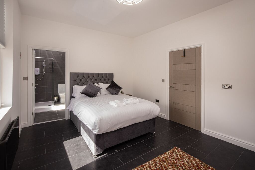 A modern bedroom with a large bed, a shower area, and a door leading to another room.