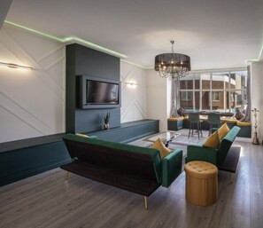 A modern living room with a flat-screen TV, green sofas, a wooden ottoman, and a chandelier. - Town View Apartment by Sasco (Blackpool)