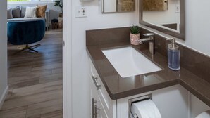 Une salle de bain moderne avec un grand miroir, un lavabo et des toilettes. On y trouve un porte-serviettes et une plante sur le comptoir.