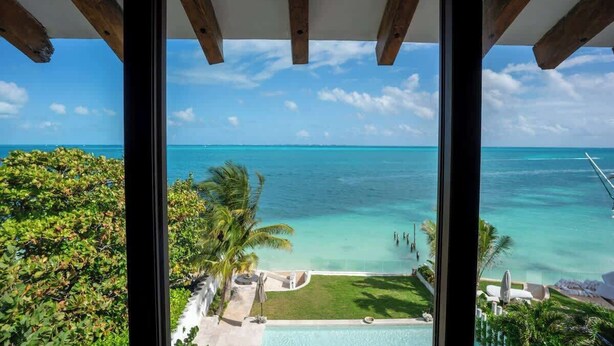 A view from a window overlooking a clear blue sea, a swimming pool, and lush greenery. - Villa Presidente | 4BR | Oceanfront Luxury Stay (Cancún)