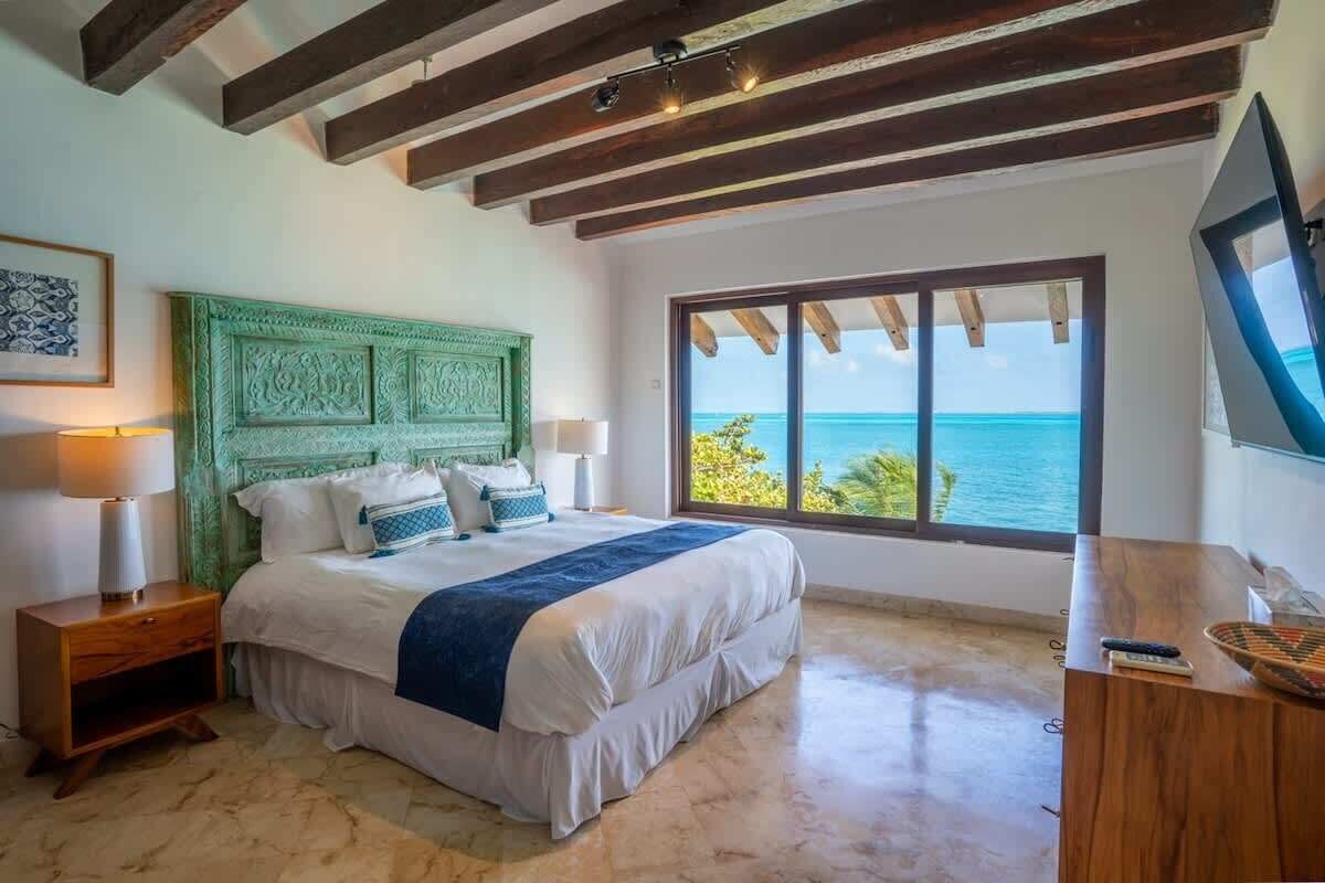 A bedroom with a large bed, a green headboard, a wooden desk, and a view of the ocean.