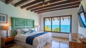 A bedroom with a large bed, a green headboard, a wooden desk, and a view of the ocean. - Villa Presidente | 4BR | Oceanfront Luxury Stay (Cancún)
