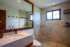 Une salle de bain dotée d’un grand miroir, d’un lavabo, de toilettes et d’une douche à parois de verre.