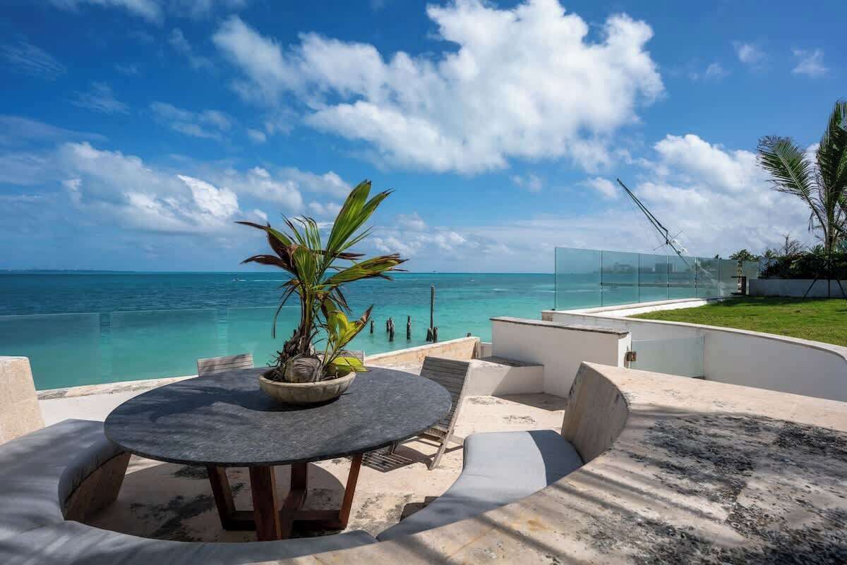 A round table with a potted plant, outdoor seating, and a view of the ocean.
