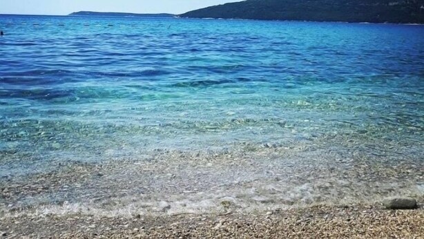 A clear view of a beach with shallow water and pebbles, a distant hill, and a clear sky. - Penthouse apartment, balcony with sea view, lift, sleeps up to 4 people (Herceg Novi)