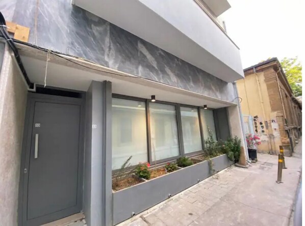 Stylish building with a flat facade and large windows, featuring a narrow entrance and adjacent sidewalk.
