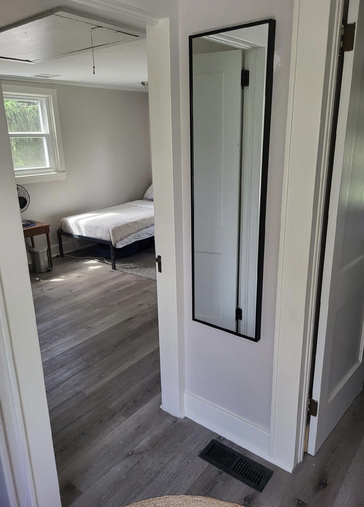 Une chambre avec un grand miroir, un lit, une table de chevet et une fenêtre.