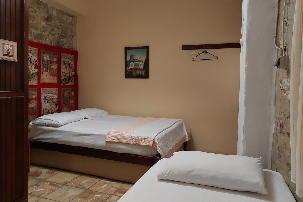 Quarto com cama, guarda-roupa de madeira, piso ladrilhado e parede com várias molduras.