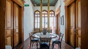 A room with a round table and chairs, wooden doors, and a green exit sign. - Ayvalık Bonjour Pansiyon (Ayvalik)