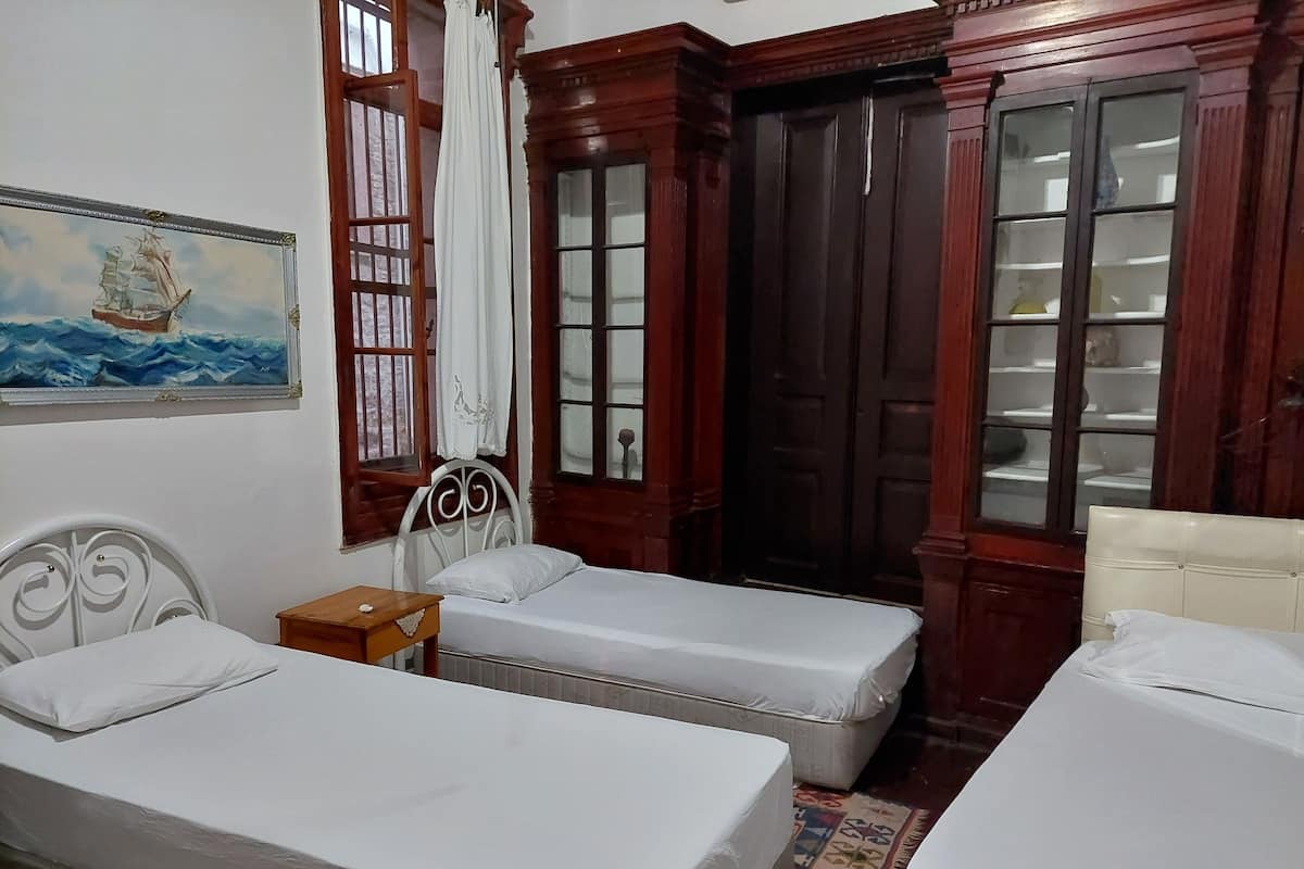 Quarto com duas camas de solteiro, um guarda-roupa de madeira e uma janela com cortinas.