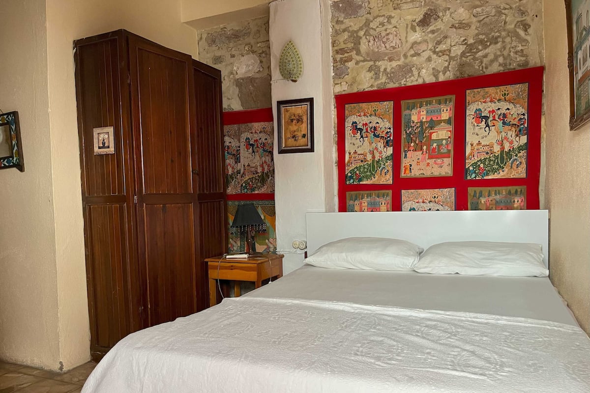 Quarto com cama grande, armário de madeira e parede decorada com pinturas coloridas.
