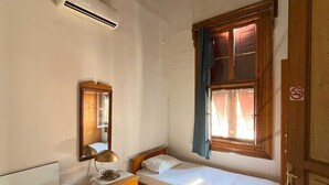 A room with two single beds, a wooden wardrobe, a mirror, a table with a lamp, and a window with curtains. - Ayvalık Bonjour Pansiyon (Ayvalik)