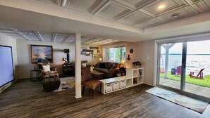 Ein gemütliches Wohnzimmer mit Kamin, bequemen Sitzgelegenheiten und einem großen Fenster mit Blick auf ein Gewässer.