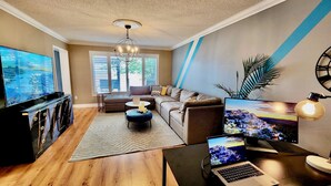 Ein modernes Wohnzimmer mit einem großen Flachbildfernseher, einer Couch, einem Couchtisch und einem Laptop auf Holzdielen.