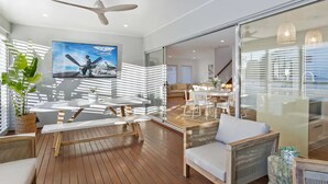 Ein modernes Wohnzimmer mit Holzboden, Deckenventilator, an der Wand montiertem Fernseher und einer Glastür, die in einen anderen Raum führt.