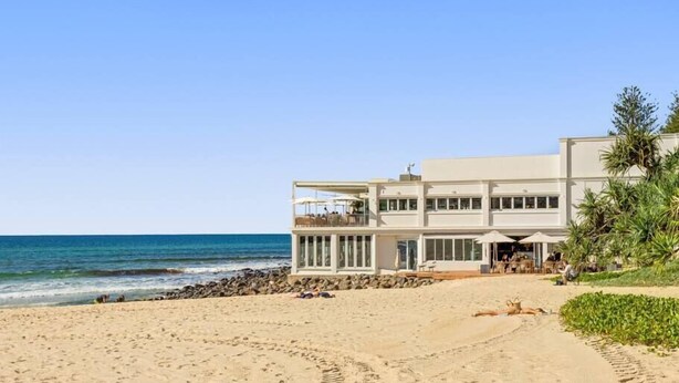 Ein Strandgrundstück mit einem großen, mehrstöckigen Gebäude, einem Sandstrand und dem Meer.