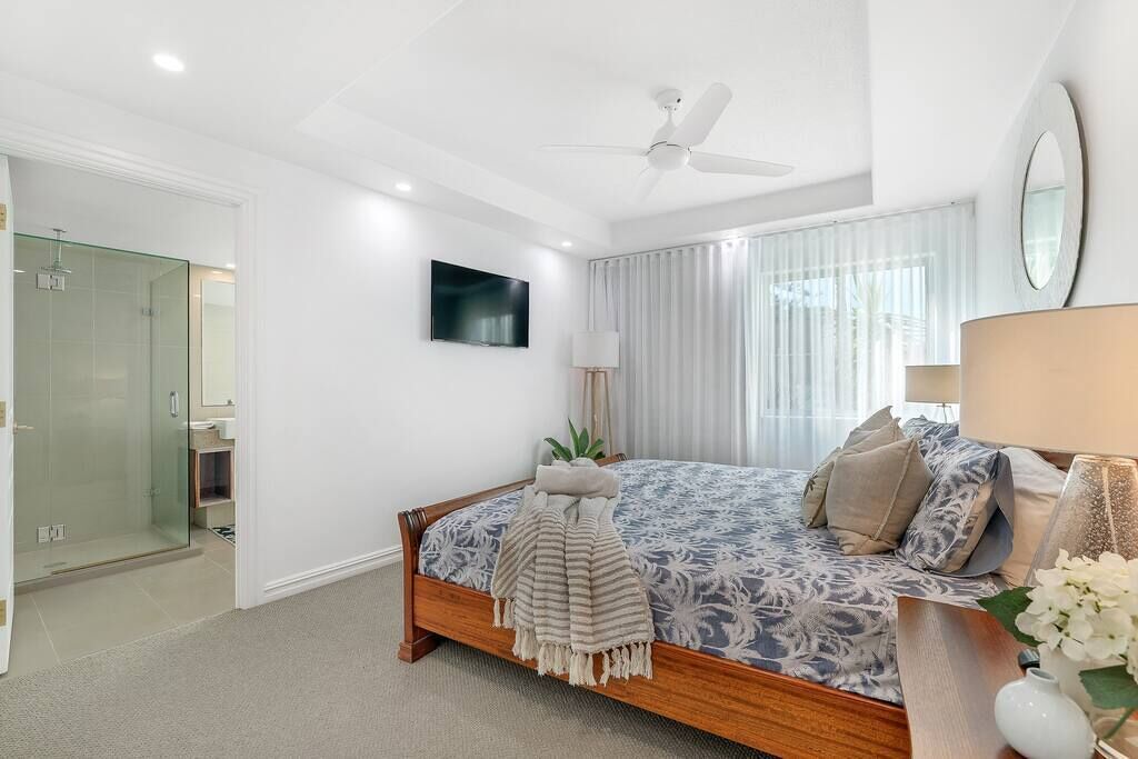 Une chambre à coucher avec un lit, un ventilateur de plafond, une télévision et une fenêtre avec des rideaux.