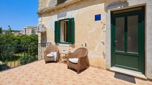 A balcony with wicker furniture, a green door, and a view of buildings in the background. - Apartment Fragola (Dubrovnik)