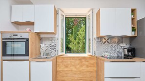 A modern kitchen with white cabinetry, a built-in oven, and a window with a view of greenery. - Apartment Fragola (Dubrovnik)