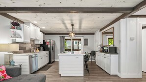 Una cocina moderna con armarios blancos, una isla central y una zona de comedor con mesa y sillas.