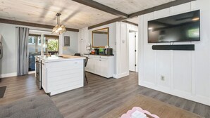 Una cocina moderna con armarios blancos, una isla central y un televisor de pantalla plana montado en la pared.