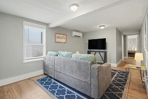 A living room with a gray sofa, a flat-screen TV, and a blue patterned rug.