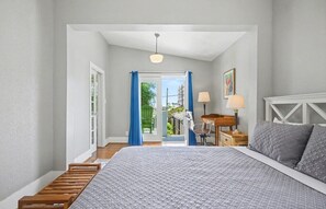 A bedroom with a bed, a desk, a chair, a lamp, and a view through a door.