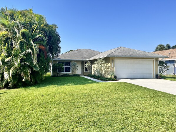 A single-story house with a garage, a lawn, and a large palm tree.