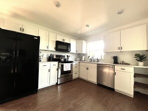 A modern kitchen with white cabinets, stainless steel appliances, and a black refrigerator.