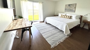 Un dormitorio con cama, escritorio, ventilador de techo, ventana con cortinas y vistas al exterior.
