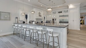 Una cocina moderna con una isla central, taburetes de bar, luces colgantes y electrodomésticos de acero inoxidable.