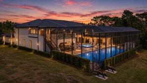 Una casa moderna con piscina, terraza techada y un amplio invernadero de vidrio.