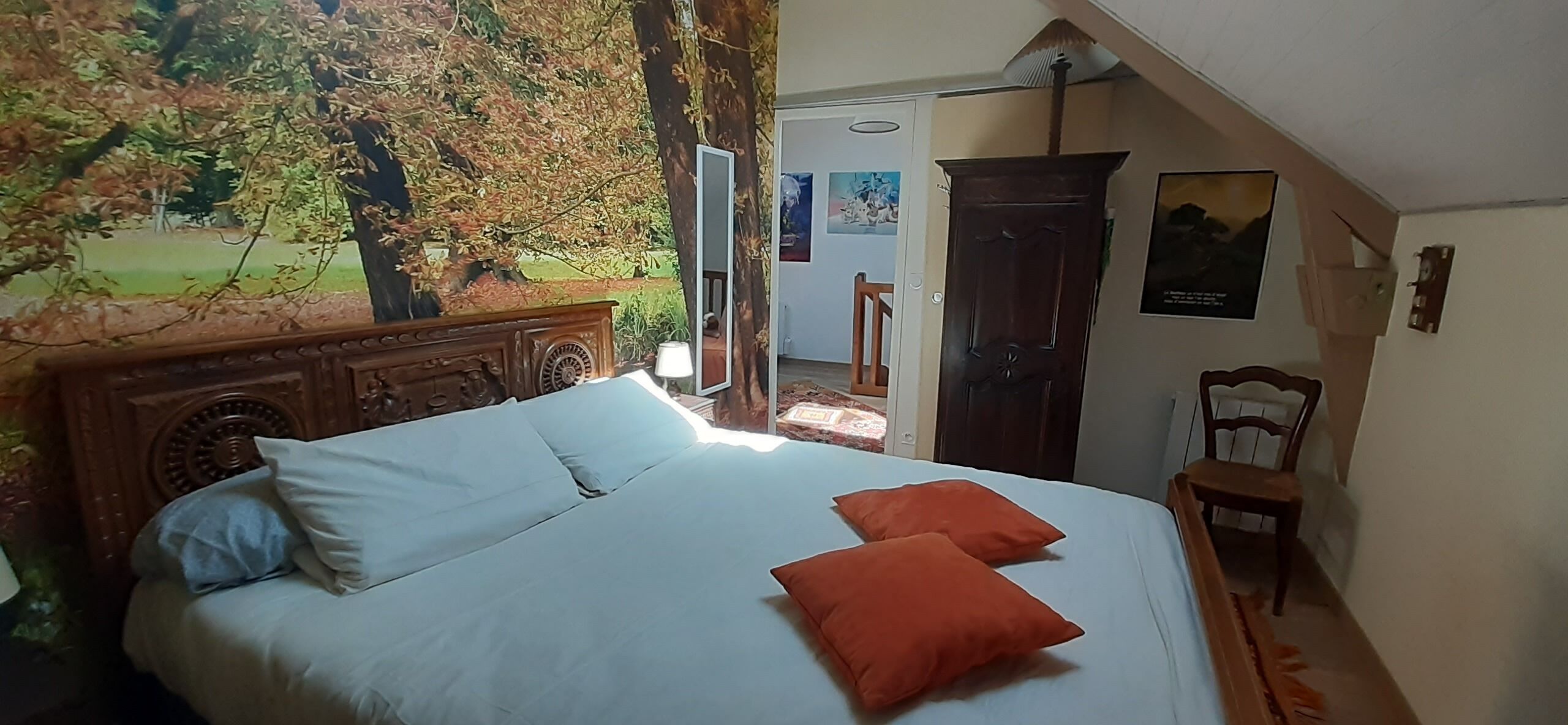 A bedroom with a bed, two pillows, a wooden headboard, a nightstand, a chair, and a door leading to a balcony.