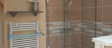Une salle de bain moderne avec une douche à parois de verre, des murs recouverts de carreaux beiges et un lavabo blanc.