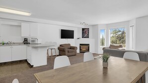 A modern kitchen with white cabinets, a flat-screen TV, a fireplace, and a dining area with a wooden table and chairs. - Steps from Perfection run.  (Beaverdell)