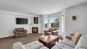 A modern living room with a fireplace, two sofas, a coffee table, and a flat-screen TV mounted on the wall. - Steps from Perfection run.  (Beaverdell)