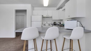 A modern kitchen with white cabinets, a white refrigerator, a stove, and a bar area with white chairs. - Steps from Perfection run.  (Beaverdell)