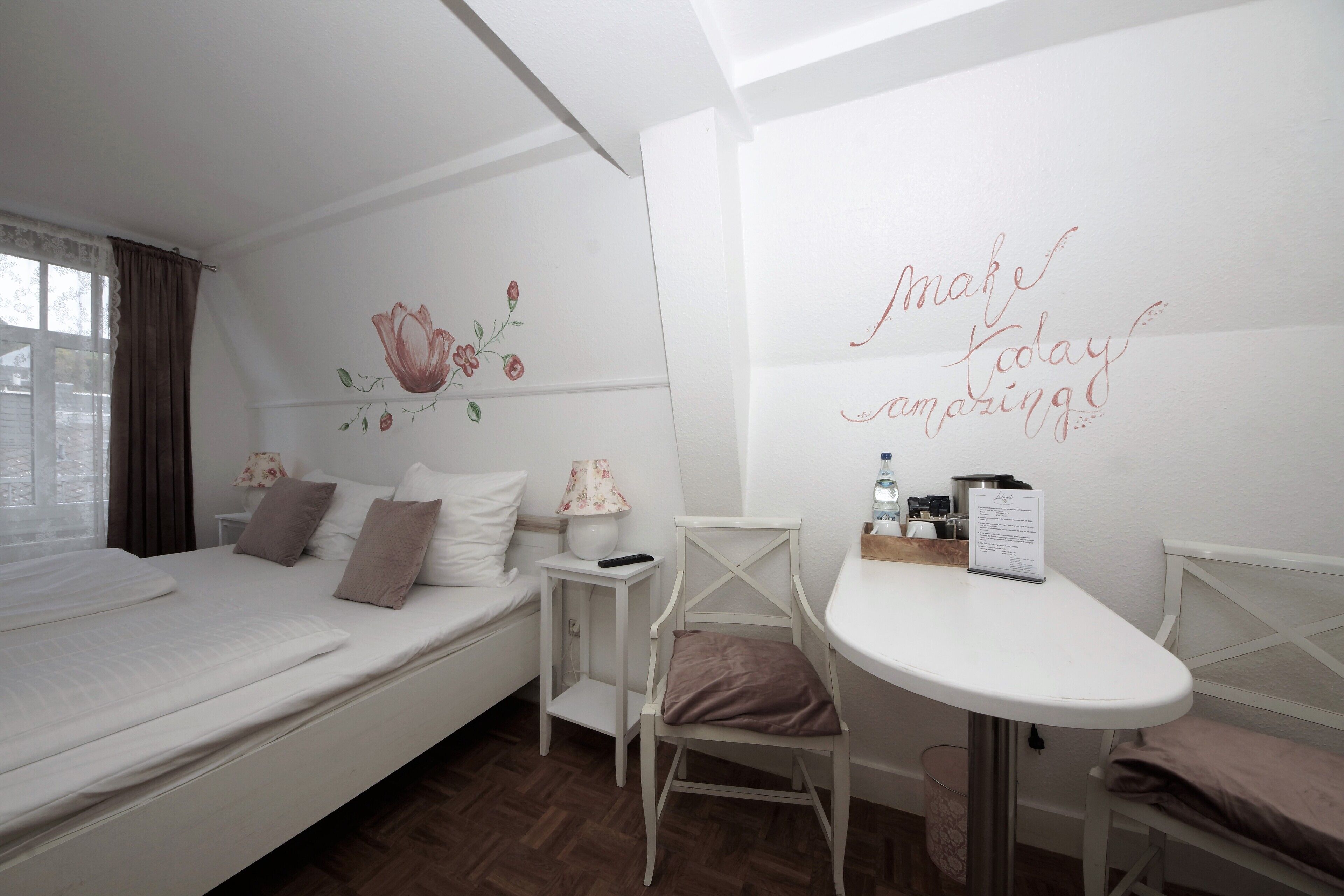 A neatly arranged bedroom with a bed, bedside table, chair, and a wall with floral artwork.