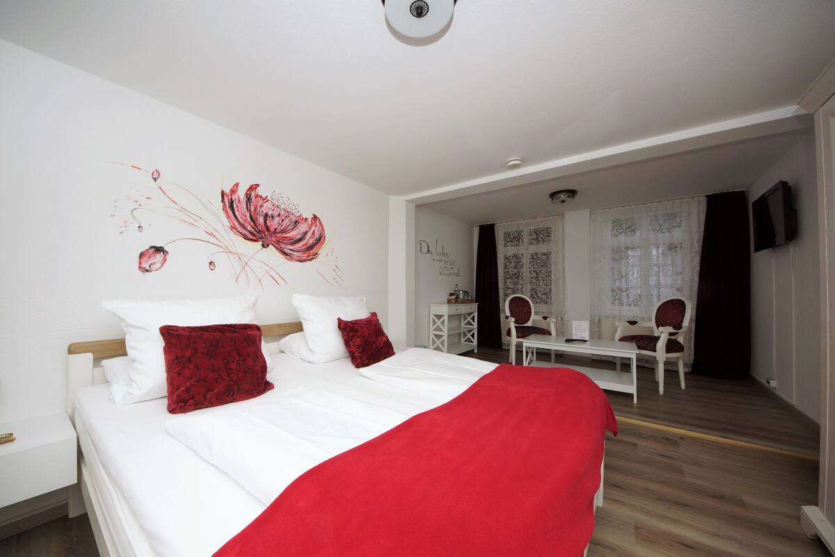 A hotel room with a bed, a desk, two chairs, a television, and a decorative wall piece.