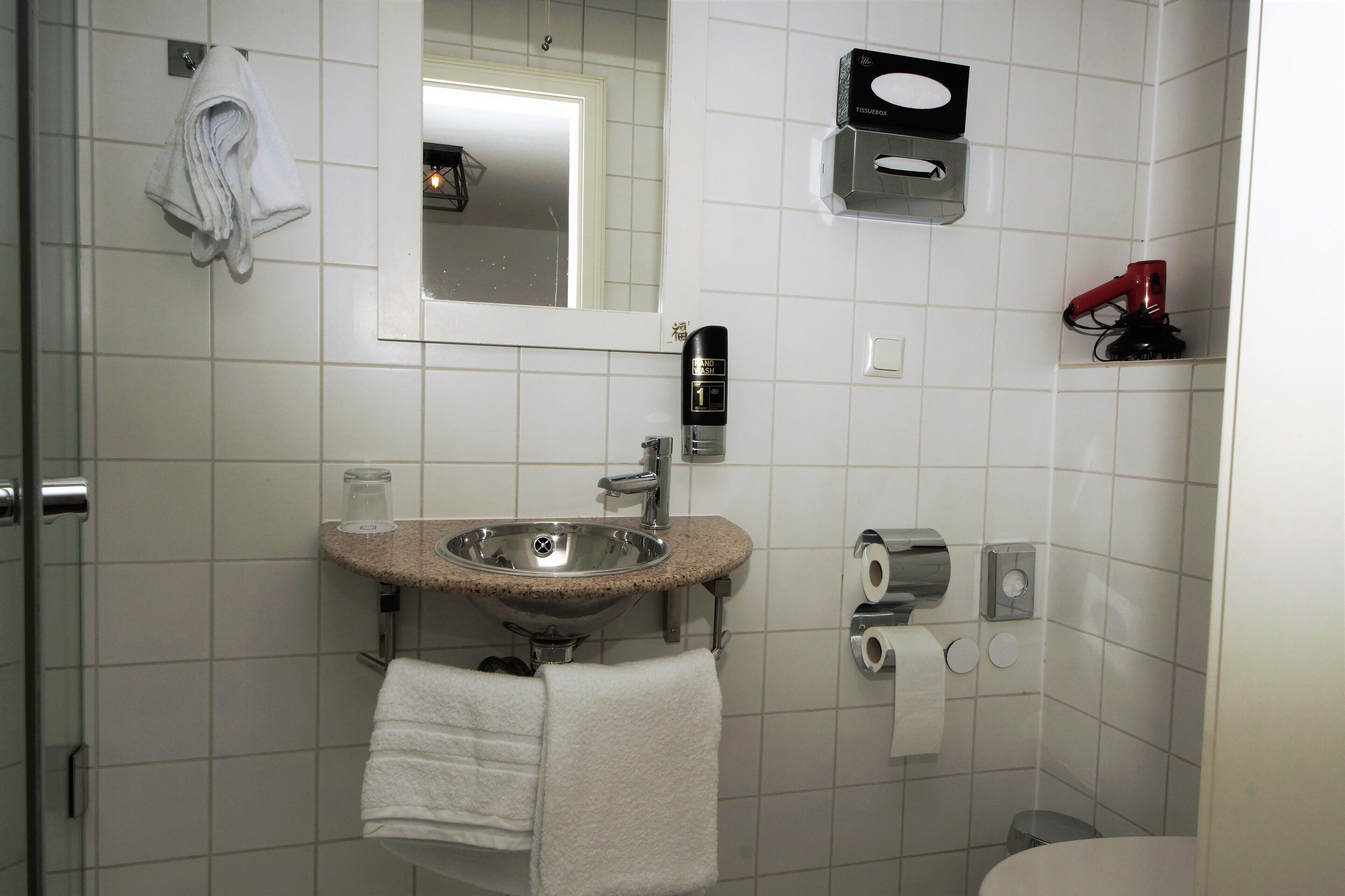 A bathroom with a sink, mirror, towel rack, and toilet paper dispenser.