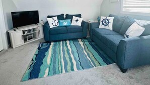 A living room with a TV, two sofas, a patterned rug, and nautical-themed pillows.